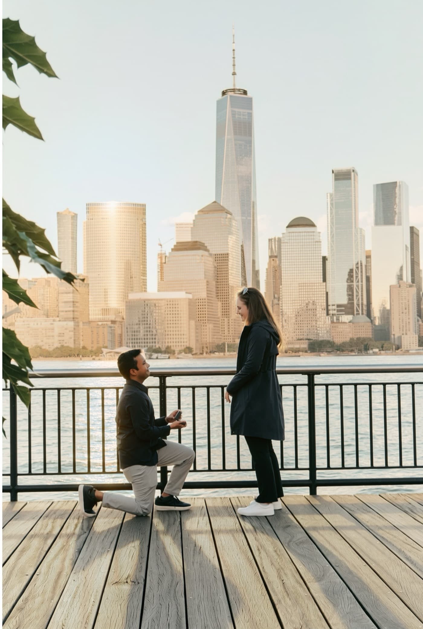 Neil proposing to Kate on the Hudson River waterfront, with the New York skyline behind them