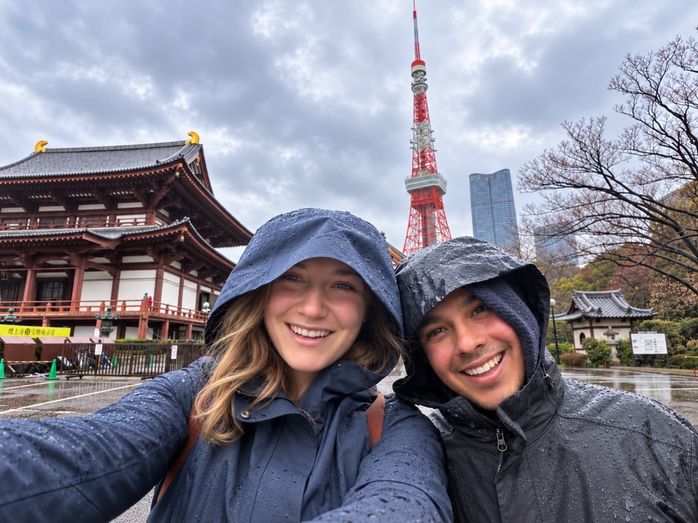 Kate and Neil in rain jackets in the pouring rain, with a Tokyo temple and Tokyo Tower behind them